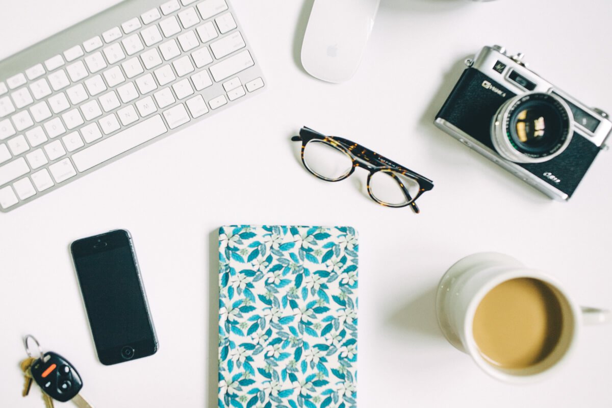 desk flat-lay with notebook, camera, glasses, and coffee